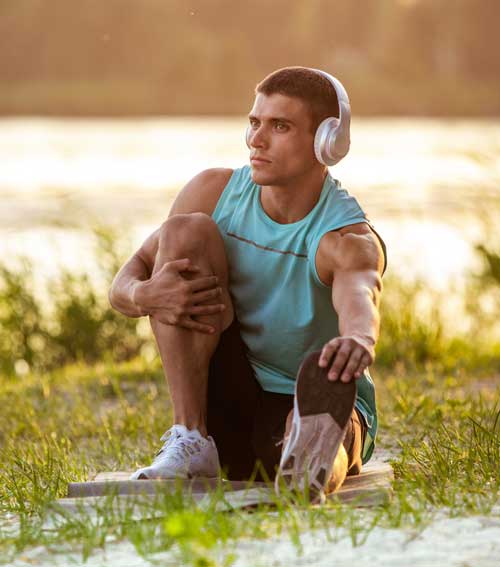 young athletic man working out listening music riverside outdoors